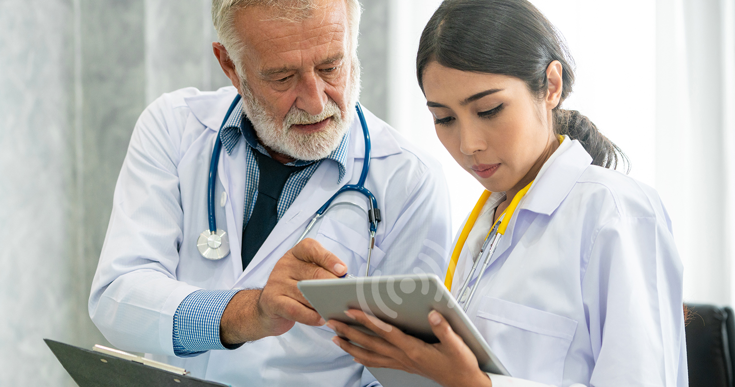Senior male doctor using tablet computer while discussing with another doctor at the hospital. Medical healthcare staff and doctor service.
