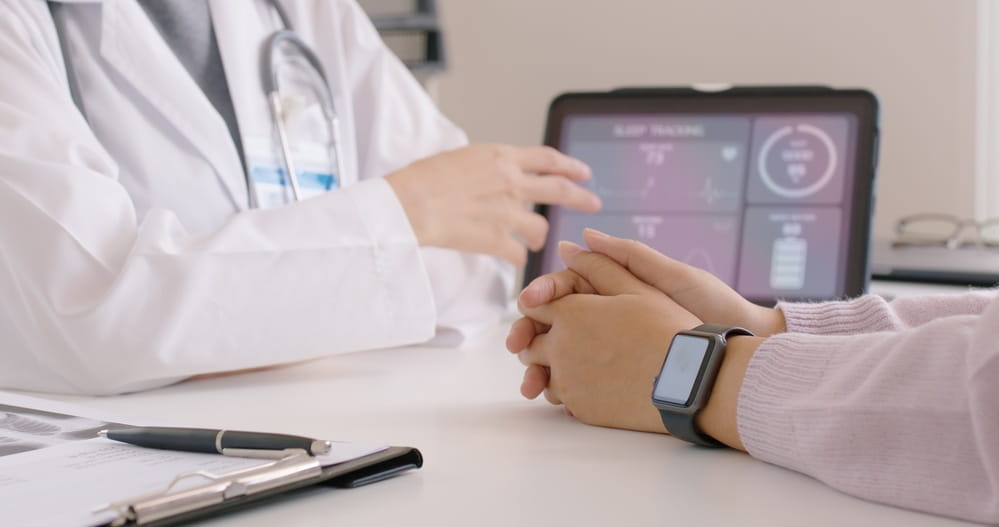 doctor pointing at data pulled from wearable medical device with patient arm wearing smart watch in foreground